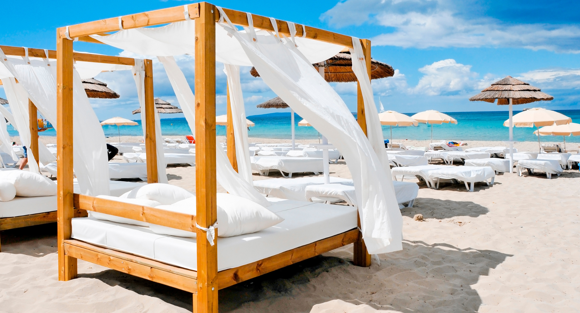 Cama balinesa con cortinas blancas en un beach club de Ibiza junto al mar